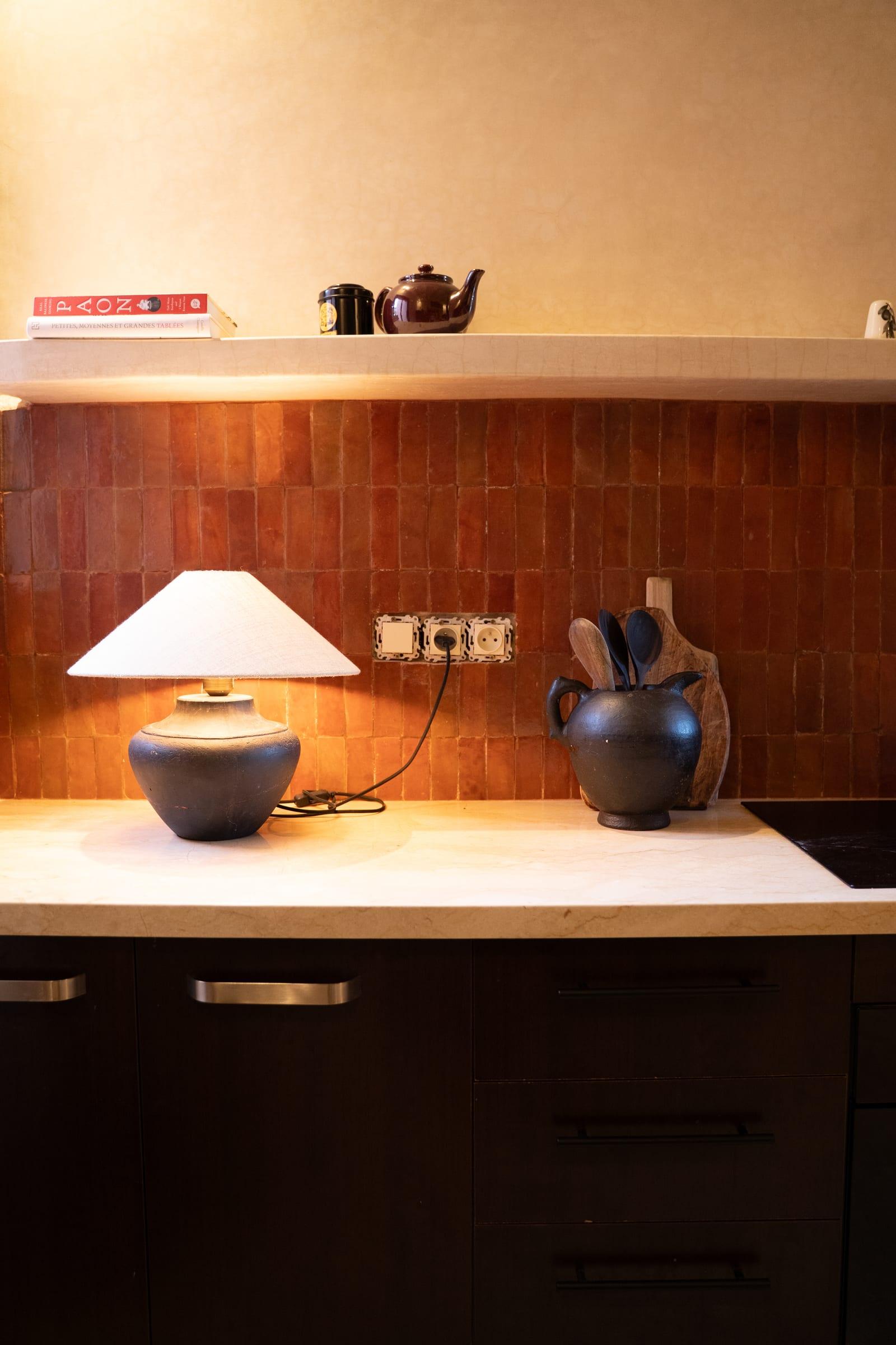 Un coin cuisine : zellige terracotta, lampe en céramique, théière sur l’étagère